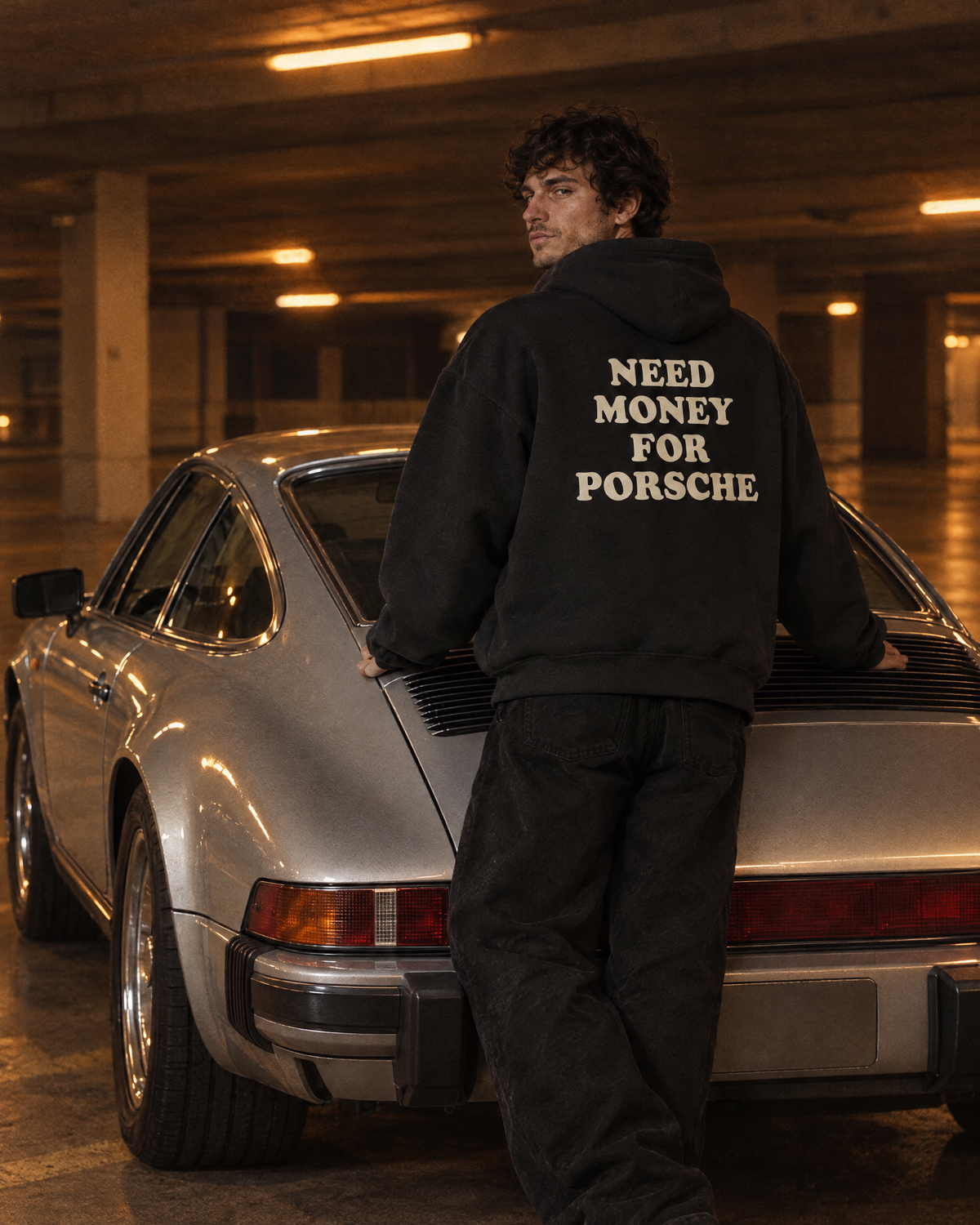 Ragazzo appoggiato a un'auto d'epoca con la felpa Need Money nera, stampa sul retro