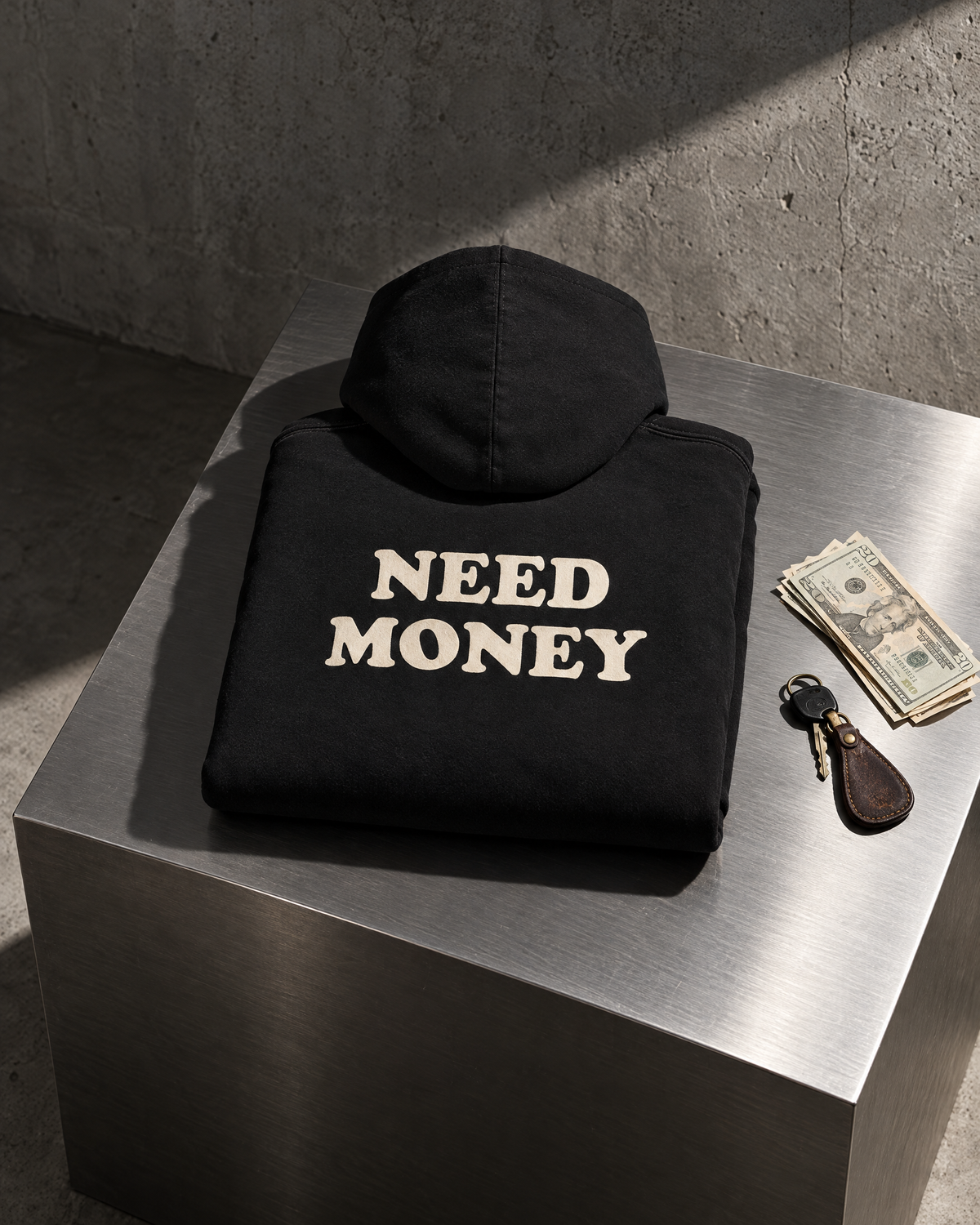 Felpa Need Money nera piegata su cubo in acciaio, stampa sul retro