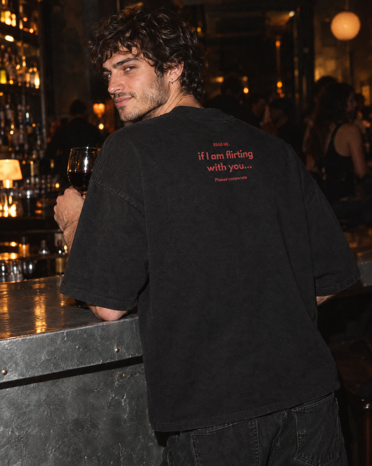 Ragazzo al bancone di un bar con la t-shirt Read Me Flirting nera, stampa sul retro
