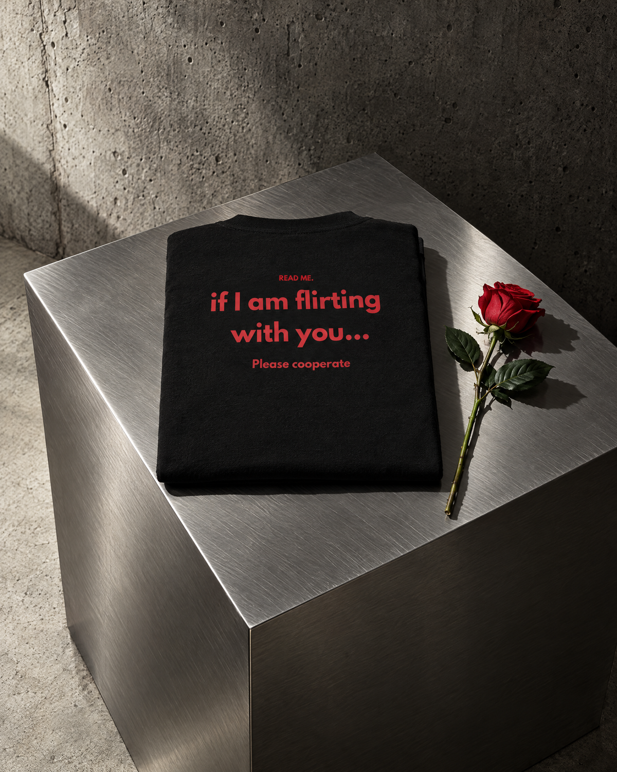 T-shirt Read Me Flirting nera piegata su cubo in acciaio con una rosa rossa